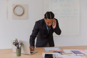 Professional businessman multitasking with phone and laptop at office desk, surrounded by documents. — Squatter Rights Wiscon