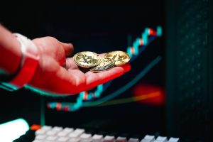 Close-up of hand holding cryptocurrency coins with trading chart in background. — The Dark Side of Exchanges: Scams and Exit